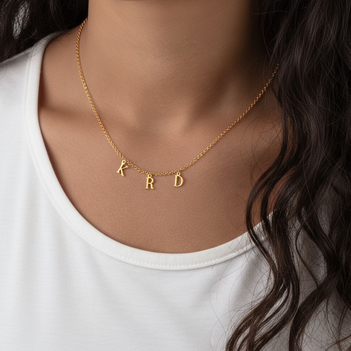 Gold necklace with 'KRD' pendant on a person wearing a white top.
